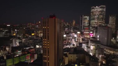 Gece şehrinde yüksek binaların etrafında uçmak. Arka planda aydınlık, modern, yüksek kuleler. Tokyo, Japonya.