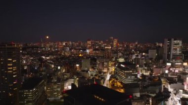 Gece metropolünün havadan panoramik görüntüsü. Büyük şehirde şehir gelişimi. Aydınlanmış binalar ve gökyüzünde ay. Tokyo, Japonya.