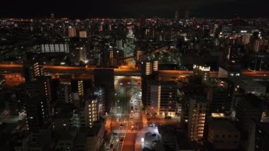 Gece şehrindeki binaların ve caddelerin üzerinden ileriye doğru uçuyor. Yükseklikten akşam metropolü. Osaka, Japonya.