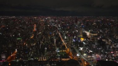 İleri, Metropolis 'in üzerinde uçuyor. Aydınlatılmış sokaklar ve büyük şehirde yüksek binalar. Osaka, Japonya.