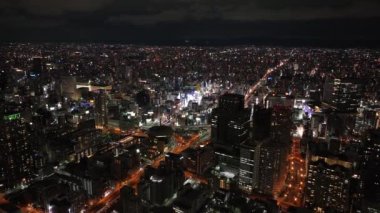 Gece büyük şehrin üzerinde uç. Geniş bir metropol alanı inşa edildi. Şehir merkezindeki çok katlı apartmanlar. Osaka, Japonya.