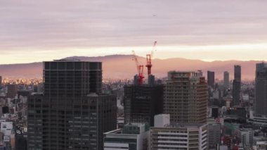 Sabahleyin büyük şehirde bir grup yüksek binalar. Bulutlu gökyüzünde parlayan güneş ışınları. İnşaatın tepesindeki vinçler. Osaka, Japonya.