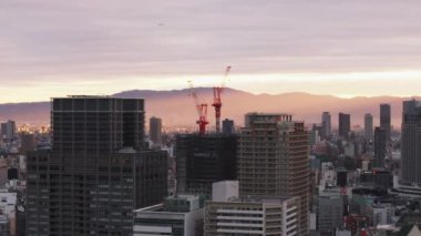 Metropolis 'teki yüksek katlı bir binanın inşaatında vinç görüntüsü. Yükselen güneş şehri aydınlatıyor ve arka plandaki tepeleri aydınlatıyor. Osaka, Japonya.
