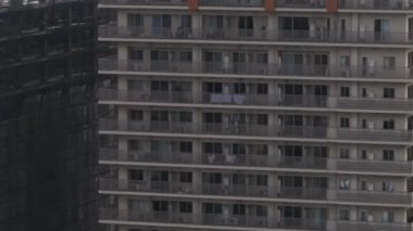 Yüksek katlı, balkonlu apartman cephesinin detaylı görüntüsü. İnşaat alanının tepesinde vinç ve arka planda şehir manzarası. Osaka, Japonya.