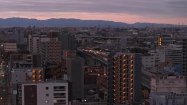 Güzel bir sabah, Metropolis 'in pembe şafak gökyüzüne karşı yükselen manzarası. Şehir merkezinden geçen cadde üzerindeki araçlar var. Osaka, Japonya.