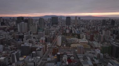 Metropolis 'in üzerinden uç. Gün doğumunda şehir merkezinde çok katlı bir bina. Bulutlar ve gökyüzündeki parlak dar şeritler. Osaka, Japonya.