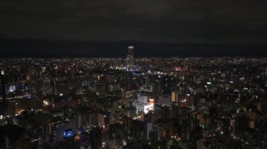 Gece büyük şehrin üzerinde uç. Şehir merkezinde çok katlı apartman binaları olan bir şehir. Uzakta bir gökdelen var. Osaka, Japonya.