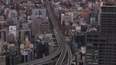 Şehirdeki yüksek anayolda giden araçların yüksek açılı görüntüsü. Güneş doğduğunda şehir manzarasını ortaya çıkar. Osaka, Japonya.