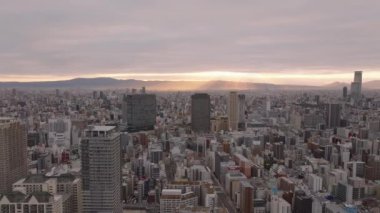 Sabahları büyük şehrin havadan panoramik görüntüsü. Bulutlu gökyüzünde parlayan güneş. Şehir merkezindeki yüksek binalar. Osaka, Japonya.