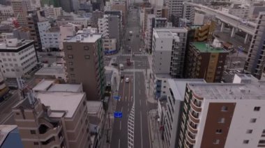 Şehir merkezindeki geniş caddenin üzerinde ilerliyorlar. Araçlar kavşaktan geçiyor. Şehirdeki çok katlı binalar. Osaka, Japonya.