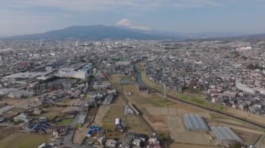 Şehrin havadan panoramik görüntüsü. Banliyöde demiryolu hattından geçen banliyö treni. İkonik Fuji Dağı uzakta. Japonya.