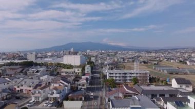 Güneşli bir günde şehrin yerleşim yerlerindeki caddenin üzerinde ilerliyorlar. İkonik Fuji Dağı bulutlarla kaplı. Japonya.