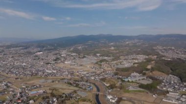 Şehrin banliyölerinin havadan panoramik manzarası. Şehir merkezindeki binalar ve ulaşım altyapısı. Dar nehir evlerin etrafında dönüyor. Japonya.