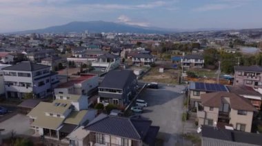 Şehir merkezindeki aile evlerinin üzerinden uç. Düz arazide bir kasaba. Uzakta kar şapkası olan görkemli Fuji Dağı. Japonya.