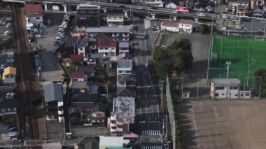 Şehir merkezindeki caddelerin ve aile evlerinin üzerinden uçuyor. Yüksek açılı binalar ve ulaşım altyapısı. Japonya.