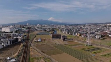 Kasabanın havadan yükselen görüntüleri. Demiryolu rayları ve nehir yerleşim yerlerindeki evler boyunca uzanıyor. Arka planda dağlar. Japonya.