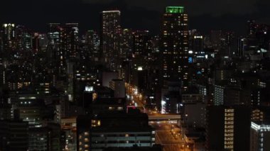 Gece şehir manzarası. Aydınlatılmış caddenin etrafında ışıklı pencereleri olan yüksek binalar. Osaka, Japonya.