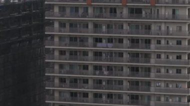 Yüksek katlı, balkonlu apartman cephesinin detaylı görüntüsü. İnşaat alanının tepesinde vinç ve arka planda şehir manzarası. Osaka, Japonya.