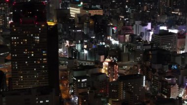 Gece şehrinin hava manzarası, ışıklı pencereli binalar ve ışıldayan gece hayatı bölgesi. Osaka, Japonya.