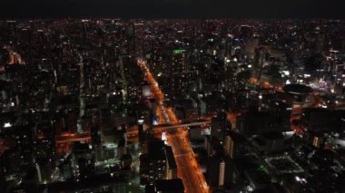 Akşam şehrinin üzerinden uç. Modern kentsel ilçede yüksek yoğunluklu kasaba gelişimi. Yol kavşağından geçen araçlara doğru eğil. Osaka, Japonya.