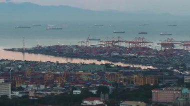 Sabah kargo limanındaki vinçlerin ve deniz aşırı konteynırların hava görüntüleri. Yüksek binaların en üst kısımları ortaya çıkıyor. Manila, Filipinler.