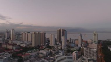 Alacakaranlıkta deniz kenarındaki çok katlı binaların hava kaydırak ve pan görüntüleri. Manila, Filipinler.