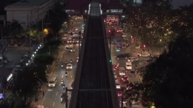 Şehirdeki ulaşım altyapısının yüksek açılı görüntüsü. Trafikle aydınlatılmış caddelerin üzerindeki çift raylı demiryolu hattı yükseltildi. Manila, Filipinler.