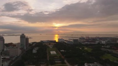 Deniz kıyısındaki şehir parkının üstünde uç. Şehirdeki yüksek binalar ve limandaki büyük vinçler günbatımının renkli gökyüzüne karşı. Manila, Filipinler.