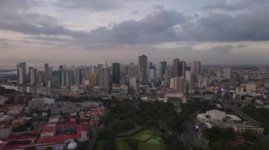 Nehir kıyısındaki modern şehir semtindeki yüksek binaların hava panoramik görüntüleri. Alacakaranlık gökyüzünde bulutlar. Manila, Filipinler.