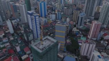 Üzerinde vinç olan yüksek binanın yüksek açılı manzarası. Eğim, yerleşim kulelerini ve gün batımını gösteriyor. Manila, Filipinler.