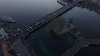 Köprüden nehrin üzerinden geçen arabaların üzerinden uçuyor. Sabahları sakin su yüzeyi. Cenevre, İsviçre.