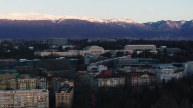 Palais des Nations 'ın havadan görünüşü ve şehir merkezindeki modern ticari binalar. Arka planda karlı dağ sırtı. Cenevre, İsviçre.