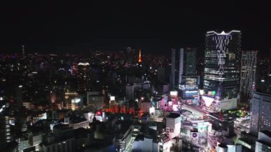 Shibuya bölgesindeki ticari merkezin hava kaydırağı ve pan görüntüleri. Parlak renkli ışıklar geceye doğru parlıyor. Tokyo, Japonya.