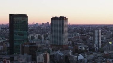 Gökyüzünün rengarenk alacakaranlık ışıklarına karşı gökdelenlerin havadan kayma ve pan görüntüleri. Parallaks etkisi. Tokyo, Japonya.