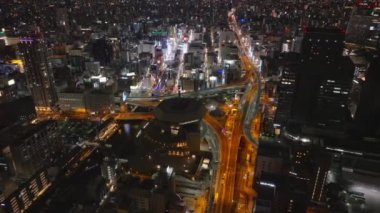 Gece şehrinin üzerinde uç. Metropolis 'te çok katlı yol kavşağından geçen arabalar. Modern şehirdeki şehir merkezinin havadan görünüşü. Osaka, Japonya.