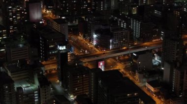 Gece şehrinin üzerinde uç. Caddelerde turuncu sokak lambalarıyla aydınlatılmış araçlar. Mahalledeki çok katlı apartmanlar. Osaka, Japonya.