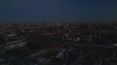 Akşam kenti üzerinde geriye doğru uç. Alacakaranlıkta Metropolis 'in havadan panoramik görüntüsü. Gökyüzüne karşı muazzam bir Fernsehturm. Berlin, Almanya.