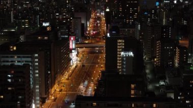 Şehirdeki geniş caddenin yüksek açılı görüntüsü. Yukarı doğru eğilince, yüksek binalarla gece manzarası ortaya çıkıyor. Osaka, Japonya.