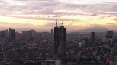 Renkli gökyüzüne karşı üzerinde vinçler olan yüksek binanın silueti. Büyük şehrin havadan görünüşü. Manila, Filipinler.