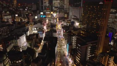 Aydınlatılmış caddelerin ve şehir merkezindeki binaların hava manzarası. Metropolis 'teki modern yüksek binalar. Şehirde yürüyen insanlar. Tokyo, Japonya.