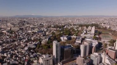 İleri, büyük şehrin üzerinde uçar. Şehir merkezlerindeki binalar ve arka plandaki dağ sırtı. Tokyo, Japonya.