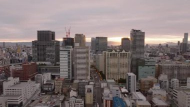 Gün doğumuna karşı yüksek binalardan oluşan bir grubun havadan görüntüsü. Metropolis 'teki şehir merkezinin üzerinden geriye doğru uçuyor. Osaka, Japonya.