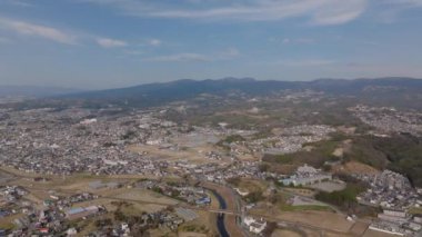 Şehrin banliyölerinin havadan panoramik manzarası. Şehir merkezindeki binalar ve ulaşım altyapısı. Dar nehir evlerin etrafında dönüyor. Japonya.