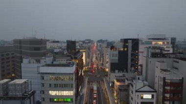 Şehir merkezindeki binaların üzerinden ileriye doğru uçuyor. Sokaktan geçen ve kavşaktan geçen araçlar. Akşam şehrinin hava manzarası. Kyoto, Japonya.