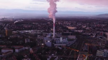 Tüten bacası olan endüstriyel banliyölerin havadan görünüşü. Alacakaranlık vakti şehrin kenar mahallelerinin panoramik manzarası. Basel, İsviçre.