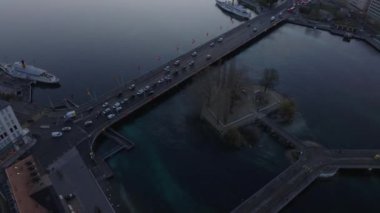 Köprüden nehrin üzerinden geçen arabaların üzerinden uçuyor. Sabahları sakin su yüzeyi. Cenevre, İsviçre.