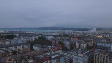 Günbatımında şehir merkezinin üzerinde ilerliyorlar. Çok katlı apartmanlar ve arka planda büyük göl. Cenevre, İsviçre.