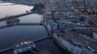 Göl kıyısındaki binaların yüksek açılı manzarası. Yukarı kaldır ve güneşin doğuşuna karşı şehrin panoramik görüntüsünü göster. Cenevre, İsviçre.