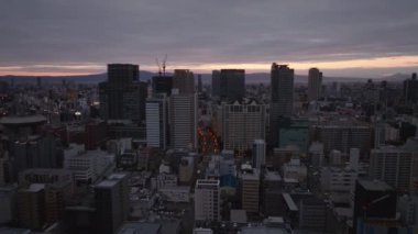 Gündoğumuna ya da günbatımına karşı modern yüksek binaların hava kaydırak ve pan görüntüleri. Alacakaranlıkta büyük şehir. Osaka, Japonya.