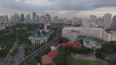 Metropolis 'teki binaların üzerinden ileriye doğru uçuyor. Belediye binasının önünden geçen bir tren. Arka planda yüksek binalar var. Manila, Filipinler.